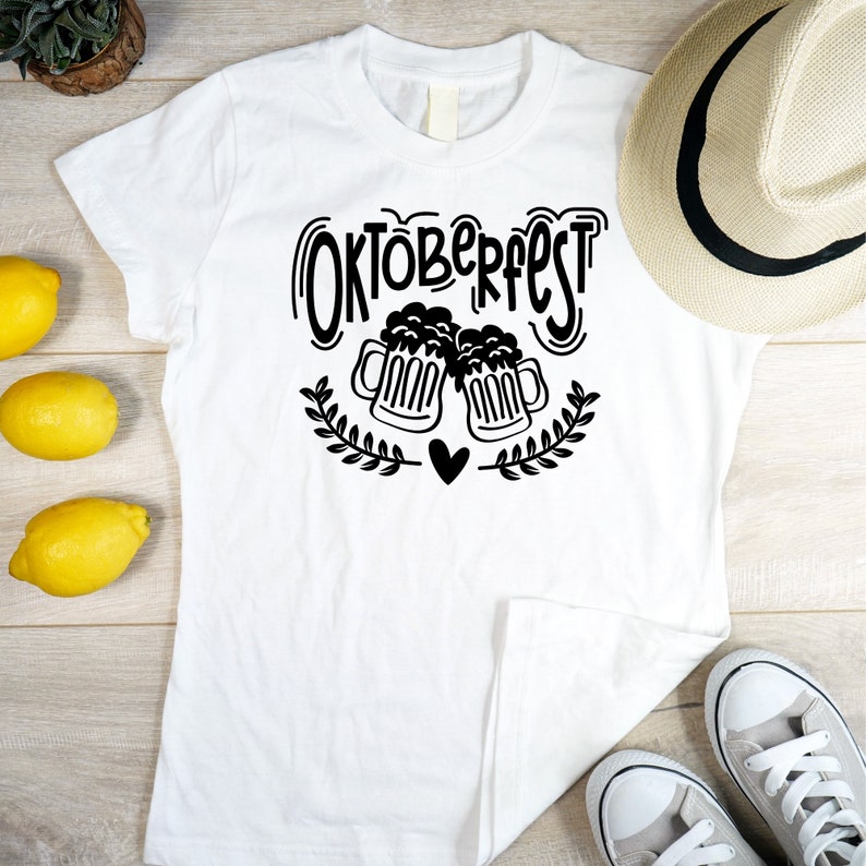 May include: White t-shirt with a black graphic design that says "Oktoberfest" with two beer mugs clinking and a heart in the middle.