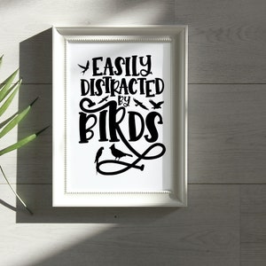Puede incluir: Impresi&oacute;n enmarcada en blanco con texto negro que dice "Easily Distracted by Birds". El texto est&aacute; en una fuente estilizada e incluye varias im&aacute;genes de siluetas de p&aacute;jaros negras.