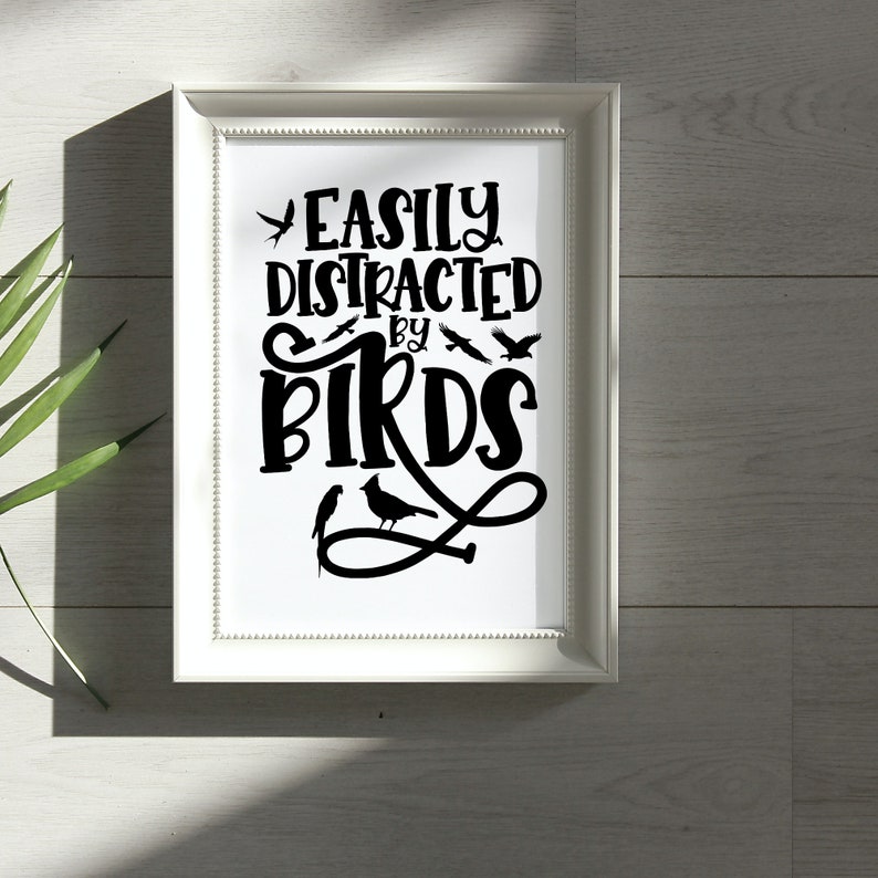 Puede incluir: Impresi&oacute;n enmarcada en blanco con texto negro que dice "Easily Distracted by Birds". El texto est&aacute; en una fuente estilizada e incluye varias im&aacute;genes de siluetas de p&aacute;jaros negras.