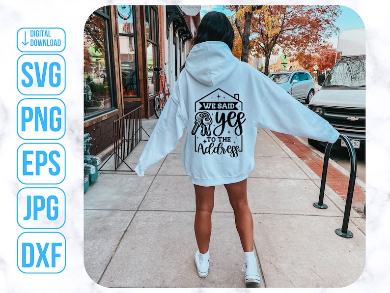 Op de afbeelding: Een witte hoodie met een zwarte afbeelding op de rug die "We said yes to the address" zegt. De afbeelding toont een huis met een sleutelgat en een sleutel.