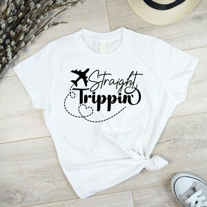 Może przedstawiać: Biała koszulka z czarnym nadrukiem samolotu i tekstem "Straight Trippin'" w stylu pisma odręcznego.