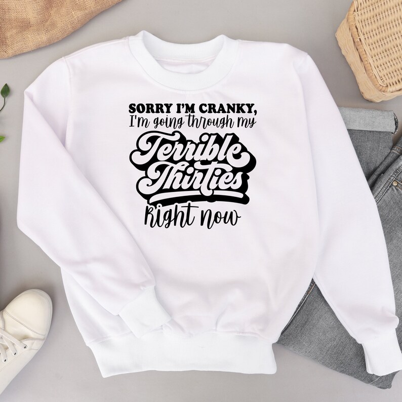 May include: White sweatshirt with black text that reads "Sorry I'm cranky, I'm going through my terrible thirties right now".