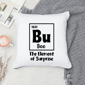 K&ouml;nnte beinhalten: Ein wei&szlig;es Kissen mit schwarzem Text, der "1031 Bu Boo The Element of Surprise" lautet. Der Text ist im Stil eines Elements des Periodensystems gestaltet.