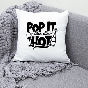 May include: White throw pillow with black text that reads "Pop It Like It's Hot" with a champagne bottle and a wine glass graphic.