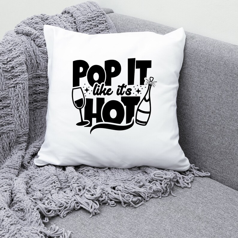 May include: White throw pillow with black text that reads "Pop It Like It's Hot" with a champagne bottle and a wine glass graphic.