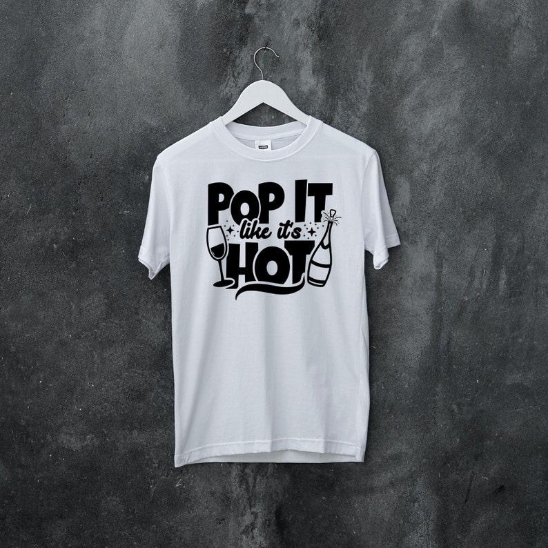 May include: White t-shirt with black text that reads "Pop It Like It's Hot" with a champagne bottle and glass graphic.