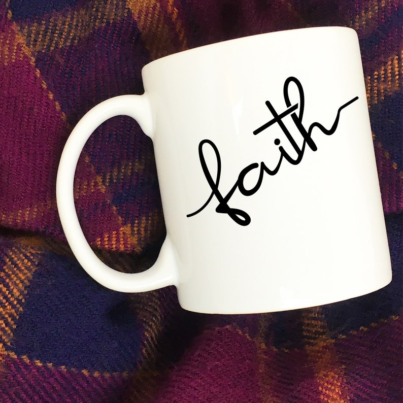 May include: White ceramic mug with a black cursive inscription that reads "faith" with a small cross above the "a".