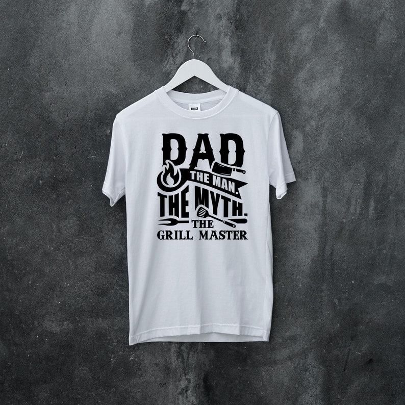 Puede incluir: Camiseta blanca con texto negro que dice "Dad The Man The Myth The Grill Master" con un gr&aacute;fico de llama y herramientas de parrilla.