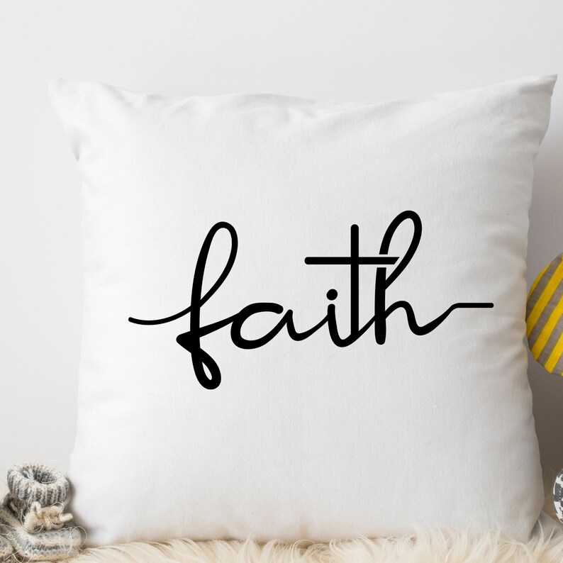 May include: White throw pillow with black cursive text that reads "faith" with a cross in the middle of the word.