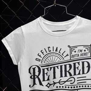 May include: White t-shirt with black text that reads "Officially Retired" with a decorative design and a small rectangle with the text "I'm Outta Here!"
