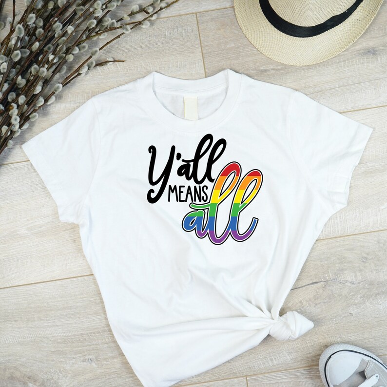 May include: White t-shirt with the text "Y'all means all" in black script. The word "all" is in rainbow colors.