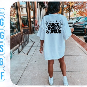 May include: A white t-shirt with black text that reads "Juice Boxes & Jesus". The shirt is being worn by a person walking down a sidewalk.