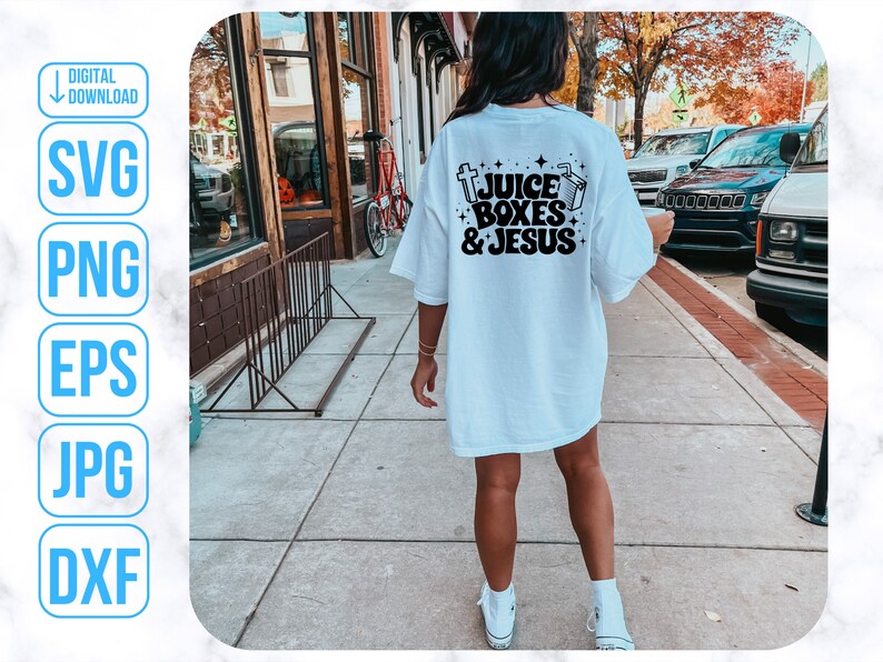 May include: A white t-shirt with black text that reads "Juice Boxes & Jesus". The shirt is being worn by a person walking down a sidewalk.