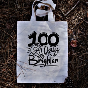 May include: White canvas tote bag with black text that reads "100 Days Brighter" and a lightbulb graphic.
