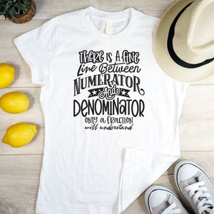 May include: White t-shirt with the text "There is a fine line between numerator and denominator. Only a fraction will understand" in black. The shirt is on a wooden surface with lemons, a hat, and sneakers.