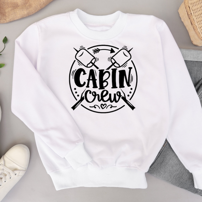 May include: White sweatshirt with a black graphic design of two crossed sticks with marshmallows on the ends. The graphic also includes a circle with the text "CABIN crew" inside.