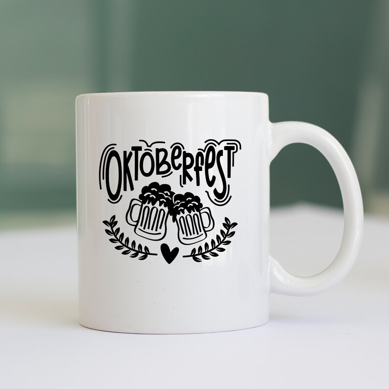May include: White ceramic mug with a black design that says "Oktoberfest" with two beer mugs clinking and a heart in the center.