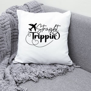 Może przedstawiać: Biała poduszka z czarnym tekstem, kt&oacute;ry brzmi "Straight Trippin'" i małą grafiką samolotu. Poduszka leży na szarej kanapie.