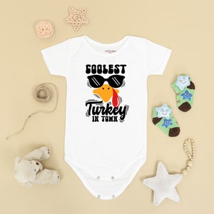 May include: White baby onesie with a cartoon turkey wearing sunglasses and the text "Coolest Turkey in Town".
