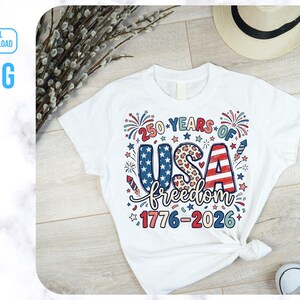 May include: White t-shirt featuring a patriotic design celebrating 250 years of USA freedom. The graphic includes the text "250 YEARS OF USA freedom 1776-2026" in red, white, and blue, with stars, fireworks, and a leopard print pattern.