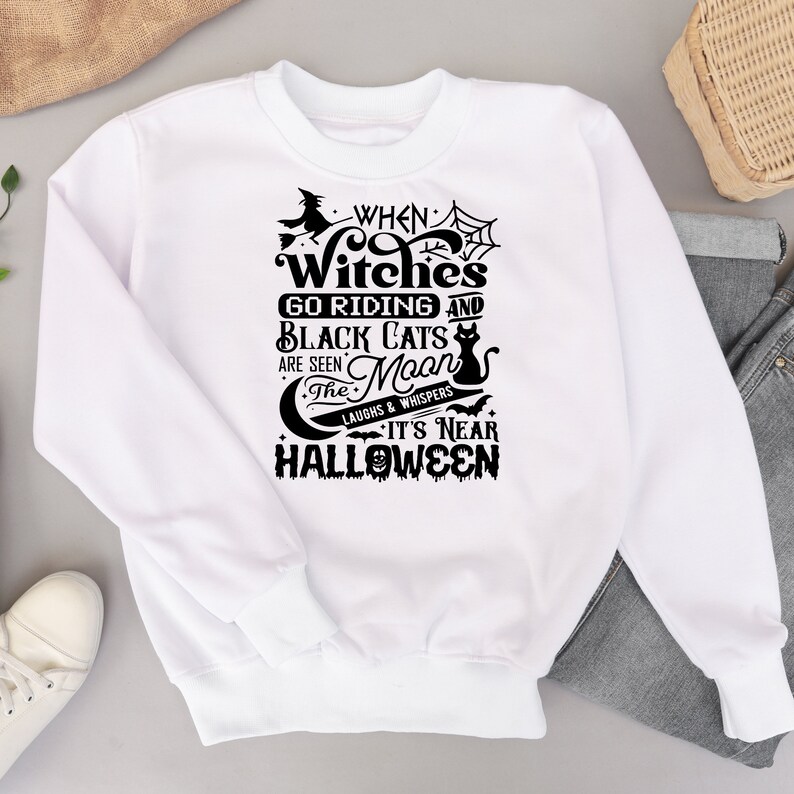K&ouml;nnte beinhalten: Wei&szlig;er Pullover mit einem schwarzen grafischen Design, auf dem steht "When Witches Go Riding and Black Cats Are Seen The Moon Laughs & Whispers It's Near Halloween".