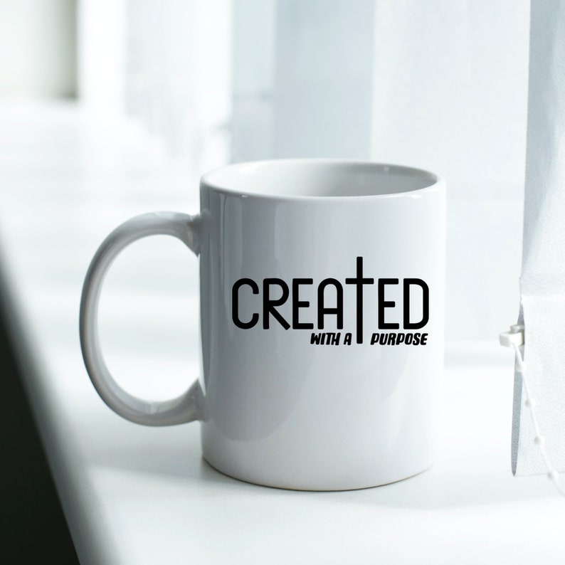 以下が含まれることがあります： 黒い文字で「CREATED WITH A PURPOSE」と黒十字が書かれた白いセラミックマグカップ