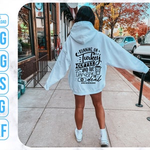 K&ouml;nnte beinhalten: Ein wei&szlig;er Hoodie mit schwarzem Text, der "Running on Turkey Coffee and the thrill of the deal #BlackFriday" lautet. Der Hoodie wird von einer Person getragen, die auf einem B&uuml;rgersteig steht.