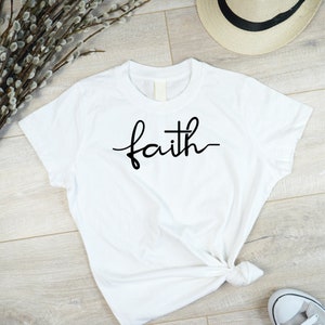 May include: White t-shirt with the word "faith" written in black cursive script.