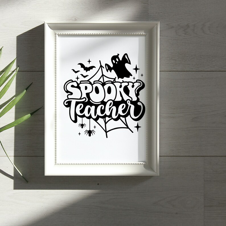 Pu&ograve; includere: Una stampa incorniciata bianca con un'illustrazione in bianco e nero di un fantasma, una ragnatela, pipistrelli e stelle. Il testo "Spooky Teacher" &egrave; scritto in un font stilizzato.