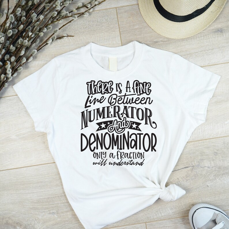 May include: White t-shirt with black text that reads "There is a fine line between numerator and denominator. Only a fraction will understand." The shirt is knotted at the bottom and is on a light wood surface.