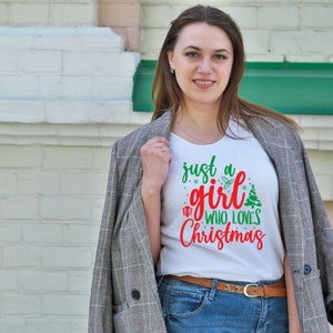 Pu&ograve; includere: Maglietta bianca con una grafica rossa e verde che dice "Just a girl who loves Christmas".