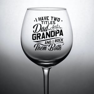 May include: A clear glass wine glass with a black vinyl decal that reads "I have two titles Dad and Grandpa and I rock them both".
