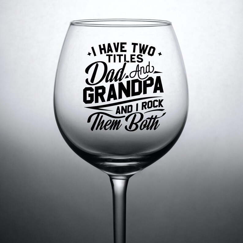 May include: A clear glass wine glass with a black vinyl decal that reads "I have two titles Dad and Grandpa and I rock them both".