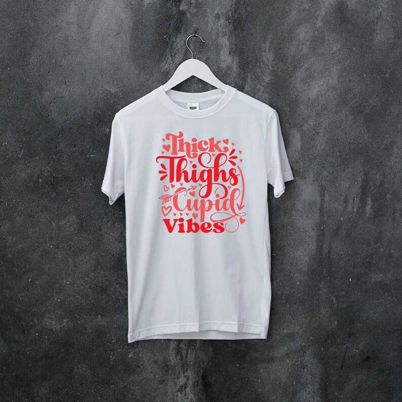 May include: White t-shirt with a red graphic that says "Thick Thighs Cupid Vibes" with hearts and arrows around the text.