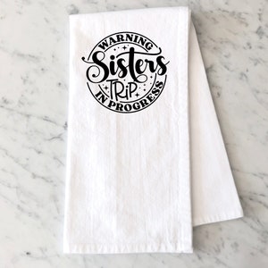 Puede incluir: Toalla de cocina blanca con texto negro que dice "Warning Sisters Trip In Progress" en un c&iacute;rculo.