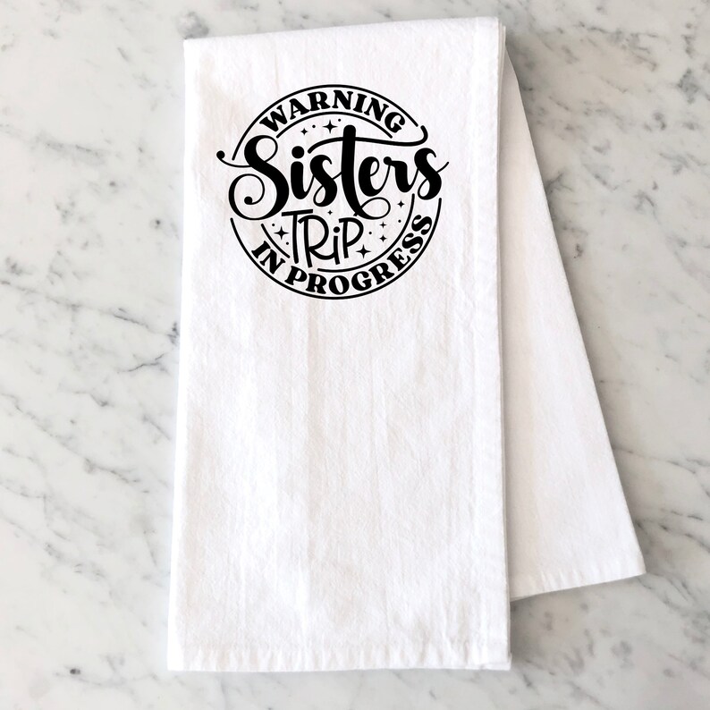 Puede incluir: Toalla de cocina blanca con texto negro que dice "Warning Sisters Trip In Progress" en un c&iacute;rculo.
