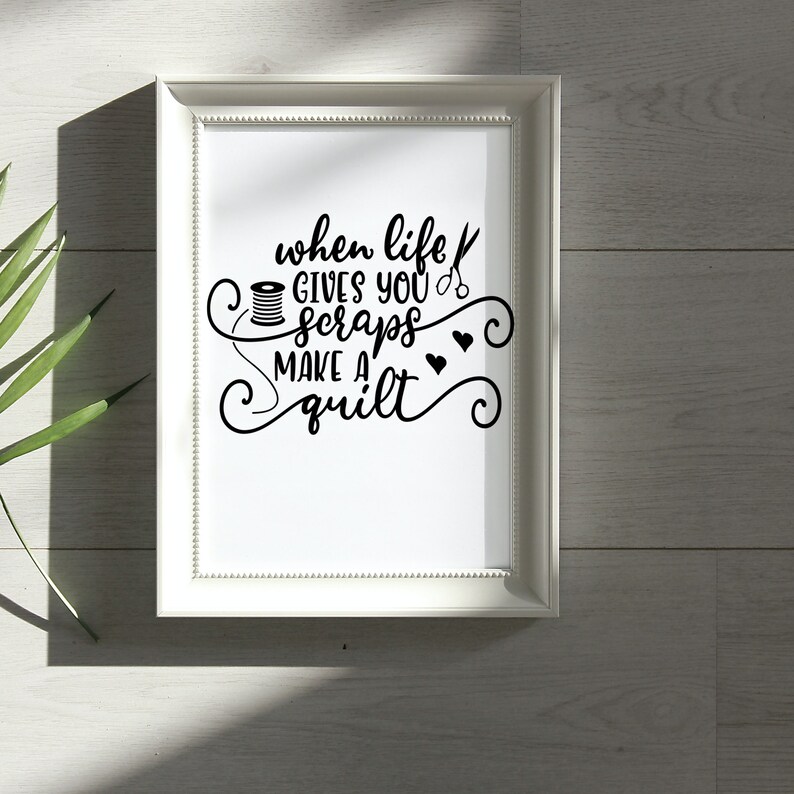 May include: White framed print with black text that reads "when life gives you scraps make a quilt". The text is surrounded by decorative swirls and includes a spool of thread and a pair of scissors.