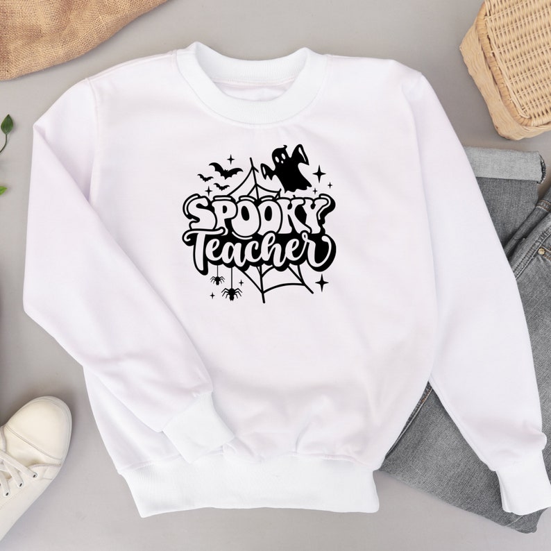 Pu&ograve; includere: Felpa bianca con un design grafico nero di un fantasma, una ragnatela e il testo "Spooky Teacher".