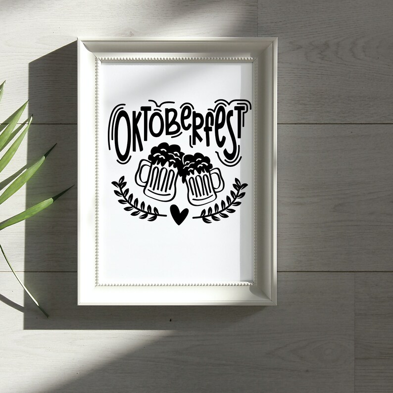 May include: A white framed print with black text that says "Oktoberfest" and a graphic of two beer steins with hearts.