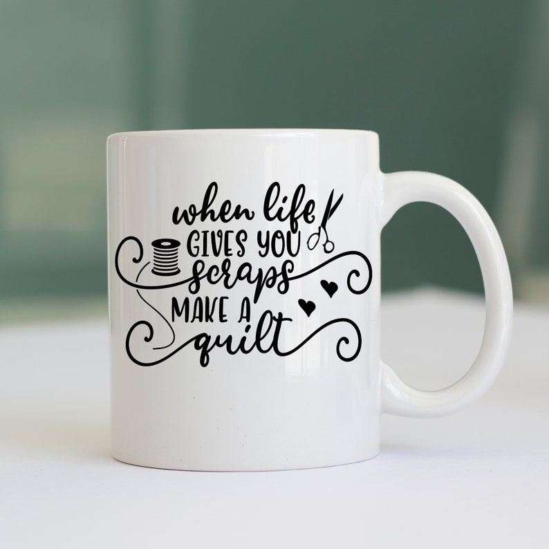 May include: White ceramic coffee mug with black text that reads "When life gives you scraps make a quilt". The text is surrounded by a decorative swirl design. There is a small image of a spool of thread and a pair of scissors.