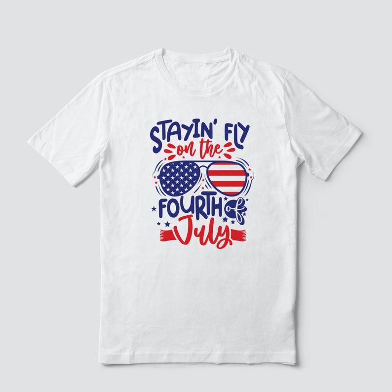 May include: White t-shirt with a red, white, and blue graphic design. The graphic features sunglasses with an American flag pattern and the text "Stayin' Fly on the Fourth of July".
