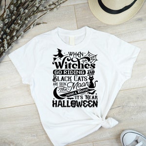 K&ouml;nnte beinhalten: Wei&szlig;es T-Shirt mit einem schwarzen grafischen Design, auf dem steht "When Witches Go Riding and Black Cats Are Seen The Moon Laughs & Whispers It's Near Halloween".