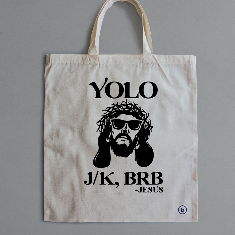 May include: A white tote bag with a black graphic of Jesus wearing sunglasses and a crown of thorns. The text "YOLO J/K, BRB -JESUS" is printed on the bag.