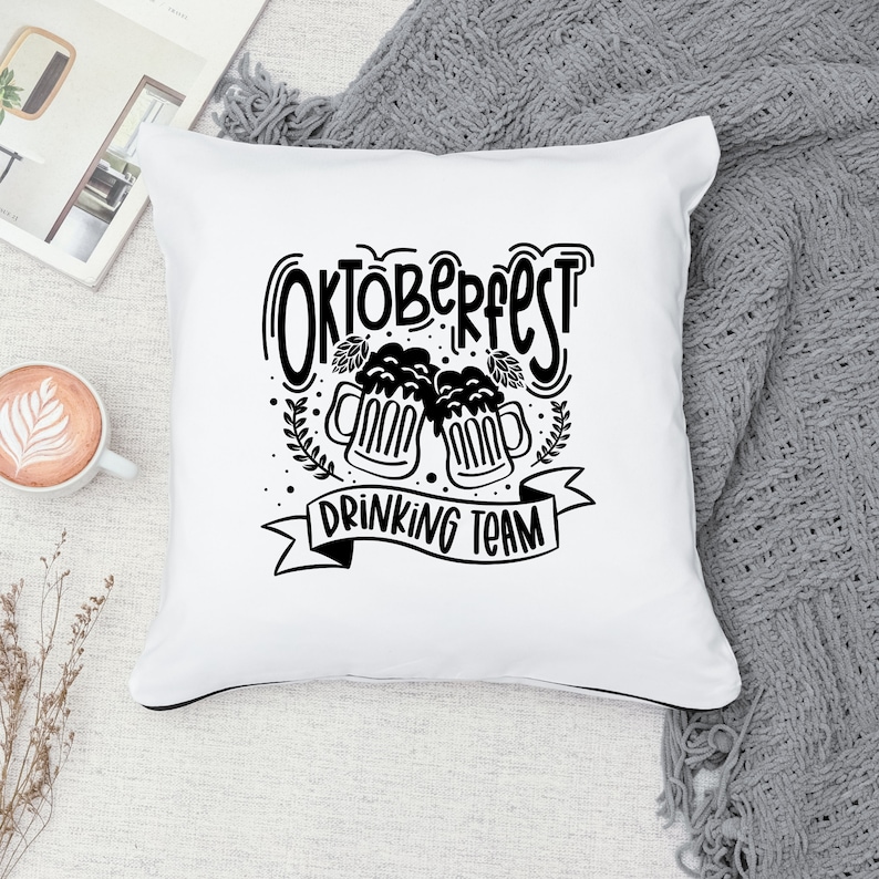 May include: White pillow with black text and graphic. The text reads "Oktoberfest Drinking Team" with a graphic of two beer steins.