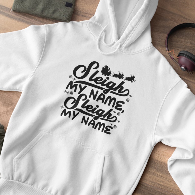 Puede incluir: Sudadera con capucha blanca con texto negro que dice "Sleigh My Name, Sleigh My Name" con un peque&ntilde;o gr&aacute;fico de Pap&aacute; Noel en un trineo con renos.