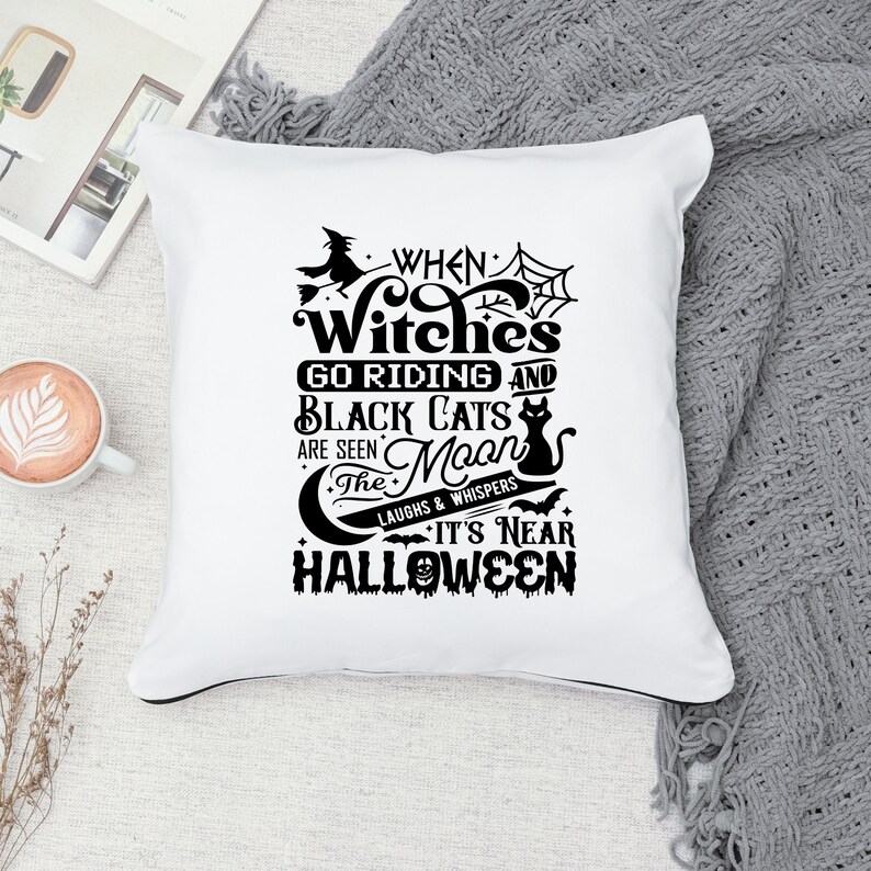 K&ouml;nnte beinhalten: Ein wei&szlig;es Kissen mit schwarzem Text, der lautet "When Witches Go Riding and Black Cats Are Seen The Moon's Laughs & Whispers It's Near Halloween". Der Text ist umgeben von einer Hexe auf einem Besen, einer schwarzen Katze, einem Halbmond und Flederm&auml;usen.