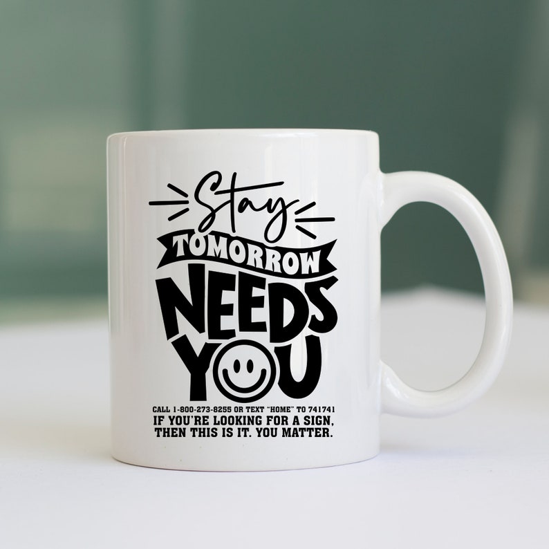 May include: White ceramic coffee mug with black text that reads "Stay Tomorrow Needs You" with a smiley face. The text also includes a phone number and a message that reads "If you're looking for a sign, then this is it. You matter."