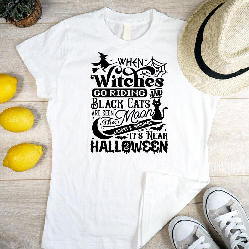 K&ouml;nnte beinhalten: Wei&szlig;es T-Shirt mit einem schwarzen grafischen Design, auf dem steht "When Witches Go Riding and Black Cats Are Seen The Moon Laughs & Whispers It's Near Halloween".