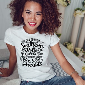 May include: A white t-shirt with a black graphic print that reads "I can go from Southern Belle to Ghetto Thug - faster than you can say - Bless your heart".
