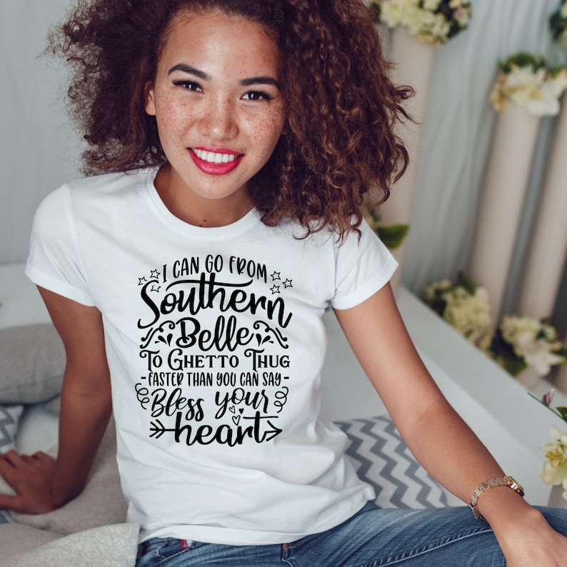 May include: A white t-shirt with a black graphic print that reads "I can go from Southern Belle to Ghetto Thug - faster than you can say - Bless your heart".